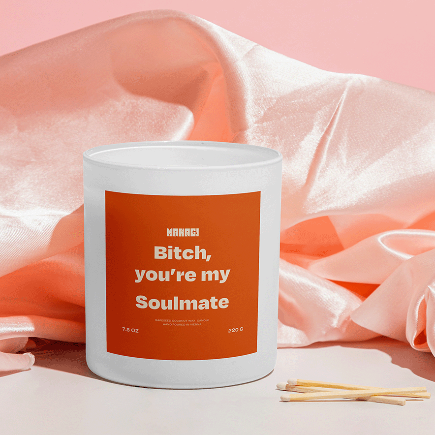 Makagi Duftkerze mit Spruch Bitch you're my soulmate stehend auf rosa Satin Hintergrund mit Streichhölzern davor