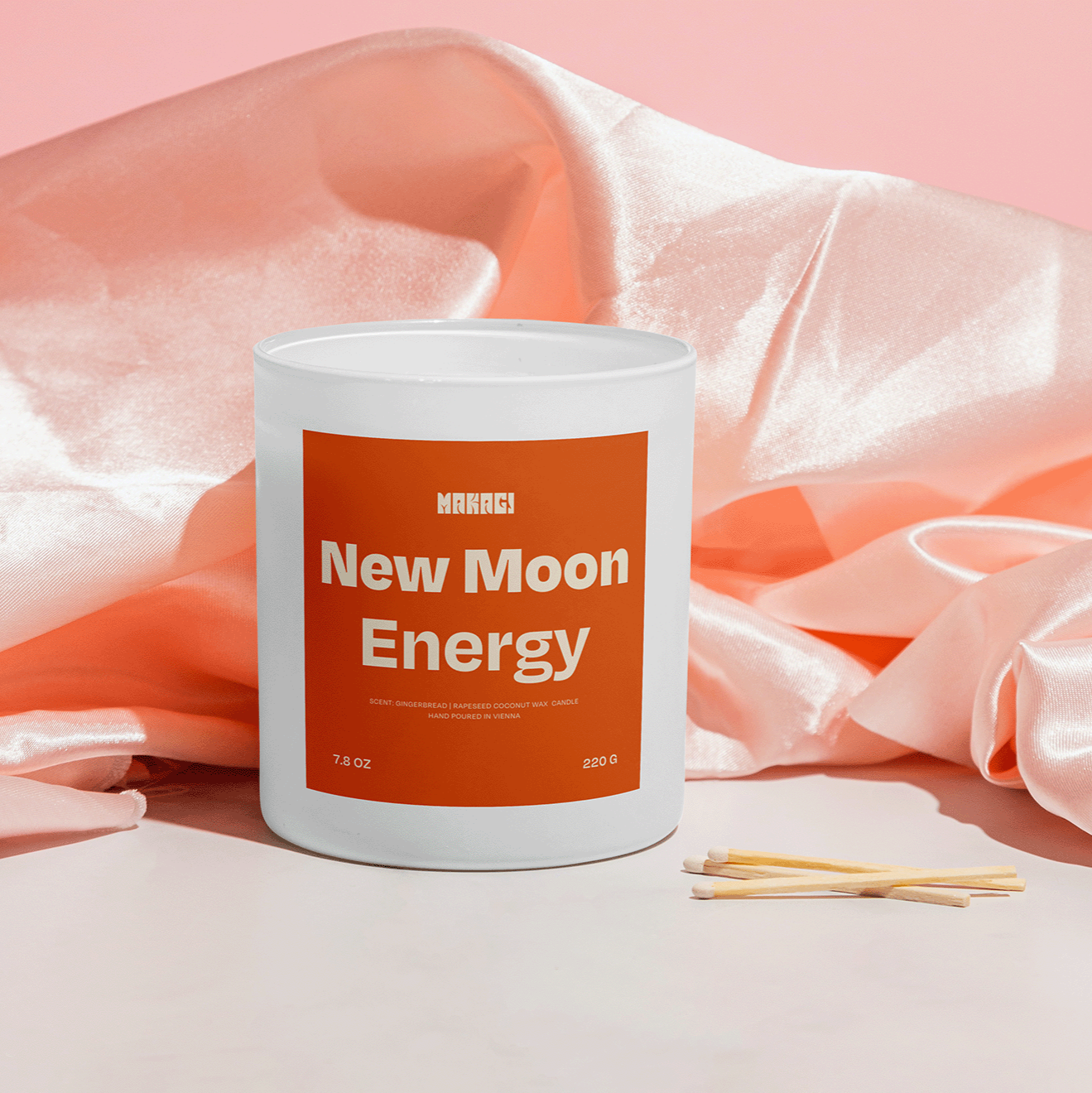 Makagi Duftkerze New Moon Energy stehend auf rosa Satin Hintergrund mit Streichhölzern davor 