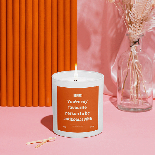 Makagi Duftkerze mit You're my favourite  person to be antisocial with stehend auf rosa Hintergrund mit Streichhölzern davor und Vase im Hintergrund