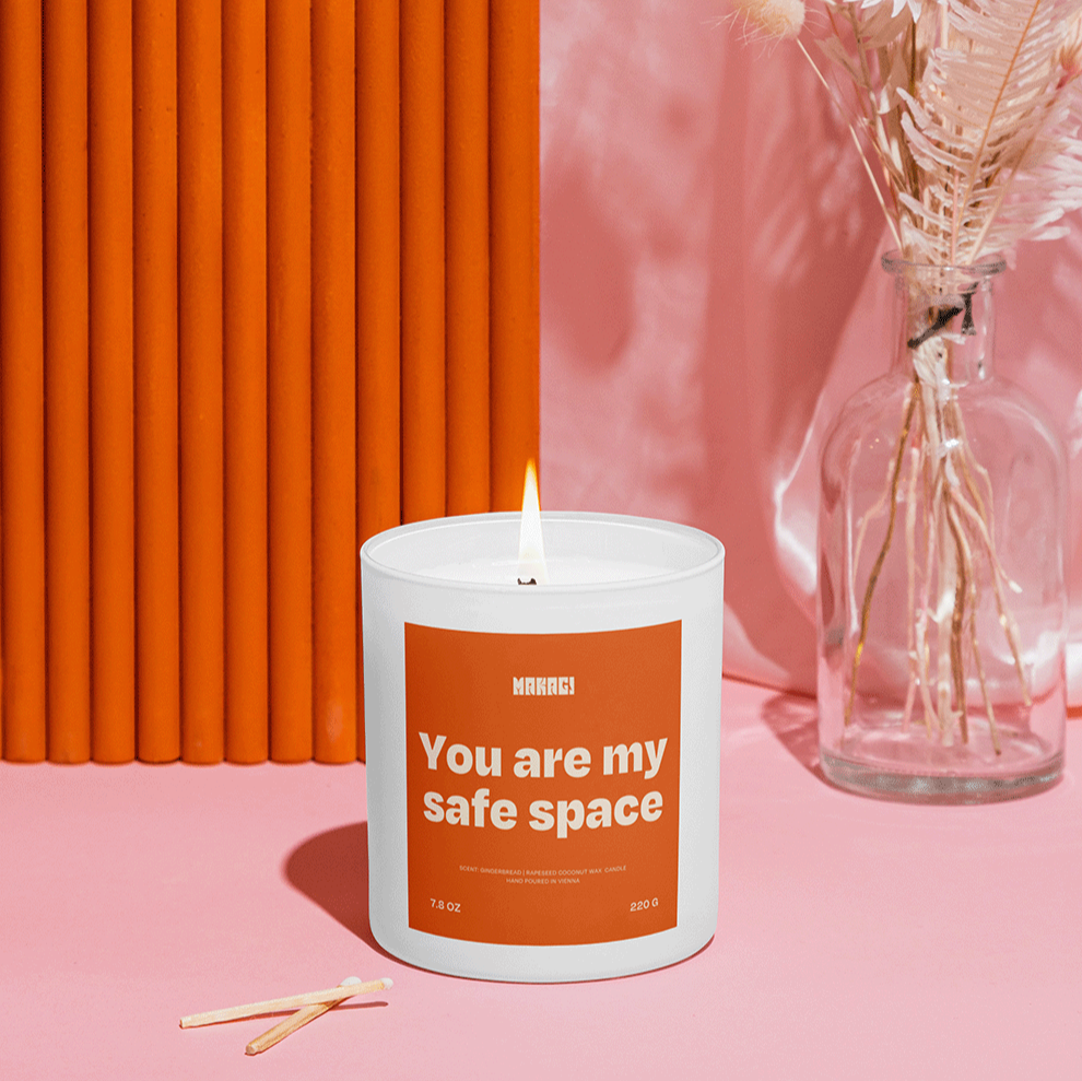 Makagi Duftkerze mit Spruch You are my safe space stehend auf rosa Hintergrund mit Streichhölzern davor und Vase im Hintergrund