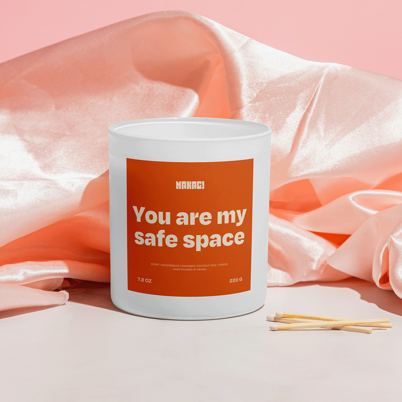 Makagi Duftkerze mit Spruch You are my safe space stehend auf rosa Satin Hintergrund mit Streichhölzern davor