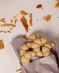 Mini-Croissant-förmige Duftwachs-Schmelzen im Duft 'Parisian Butter', elegant in einer zarten Verpackung aus Papier eingefasst, mit Bröseln von Croissant umgeben. Diese handgefertigten Wachsmelts fangen den warmen, köstlichen Duft frisch gebackener Croissants ein und bringen französisches Flair in dein Zuhause.